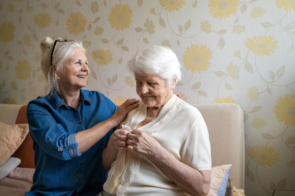 Woman helping senior woman dress in her bedroom