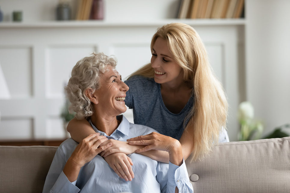 Overjoyed senior 60s mother and adult daughter relax together in living room hugging and cuddling, happy mature mum and grownup girl embrace show love enjoy home family weekend together